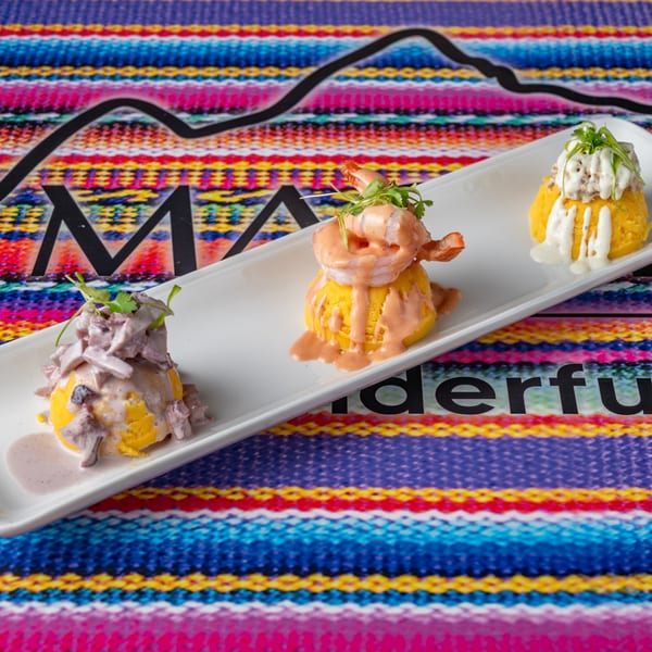 Three Peruvian causa dishes with various toppings on a white rectangular plate.