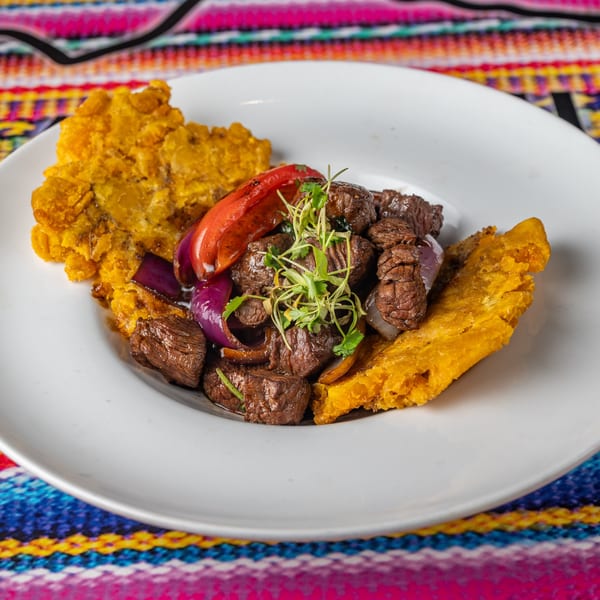 Peruvian Lomo Saltado with beef, red onions, bell peppers, and plantains on a white plate.
