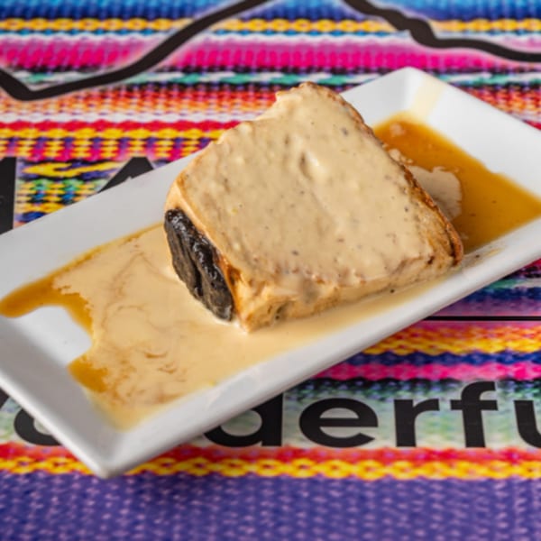 A slice of Peruvian bread pudding with a creamy sauce on a white rectangular plate.