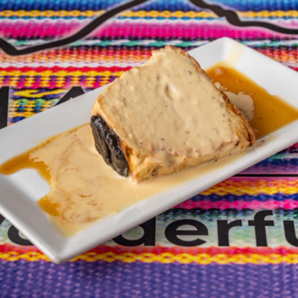 A slice of Peruvian bread pudding with a creamy sauce on a white rectangular plate.