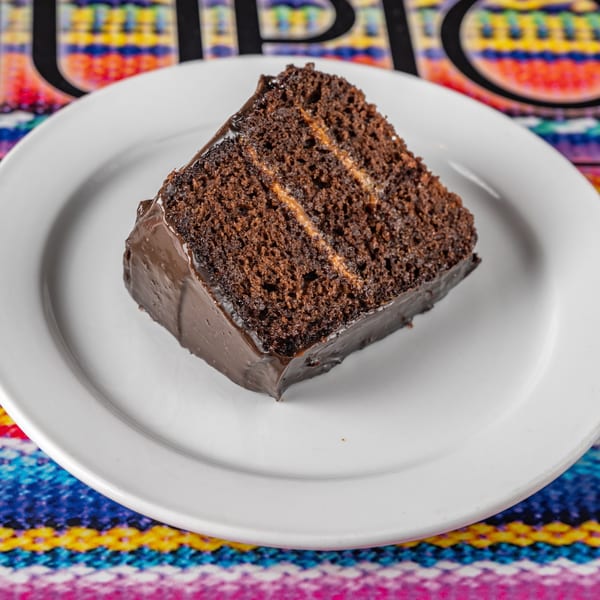 A slice of chocolate cake with dulce de leche filling on a white plate, against a colorful Peruvian textile.