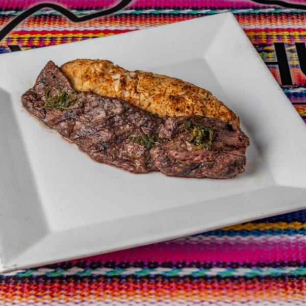 Grilled steak with herbs and rice on a white plate, set on a colorful Peruvian textile.