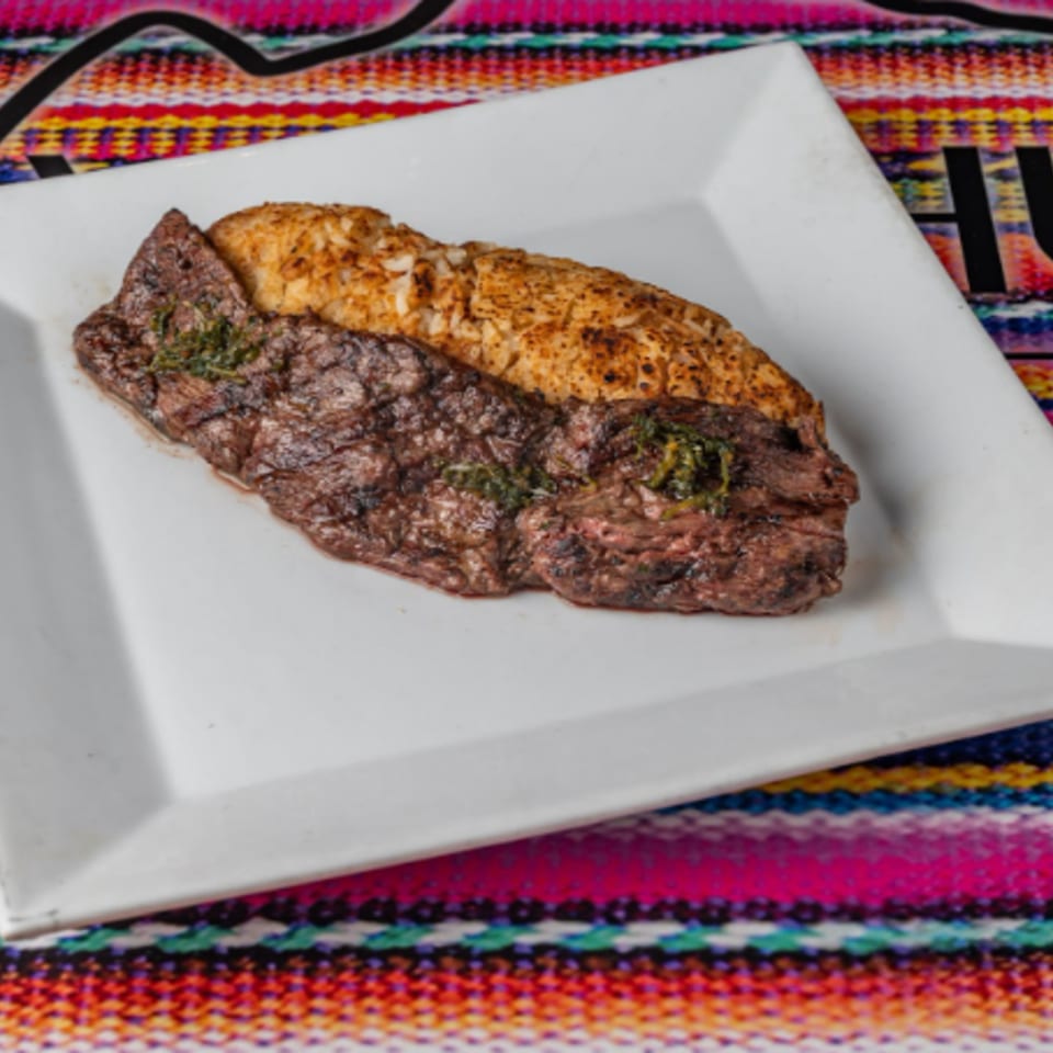 Grilled steak with herbs and rice on a white plate, set on a colorful Peruvian textile.