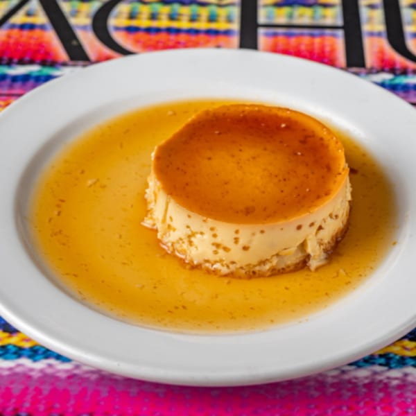 Peruvian flan dessert with caramel sauce on a white plate, against a colorful patterned background.